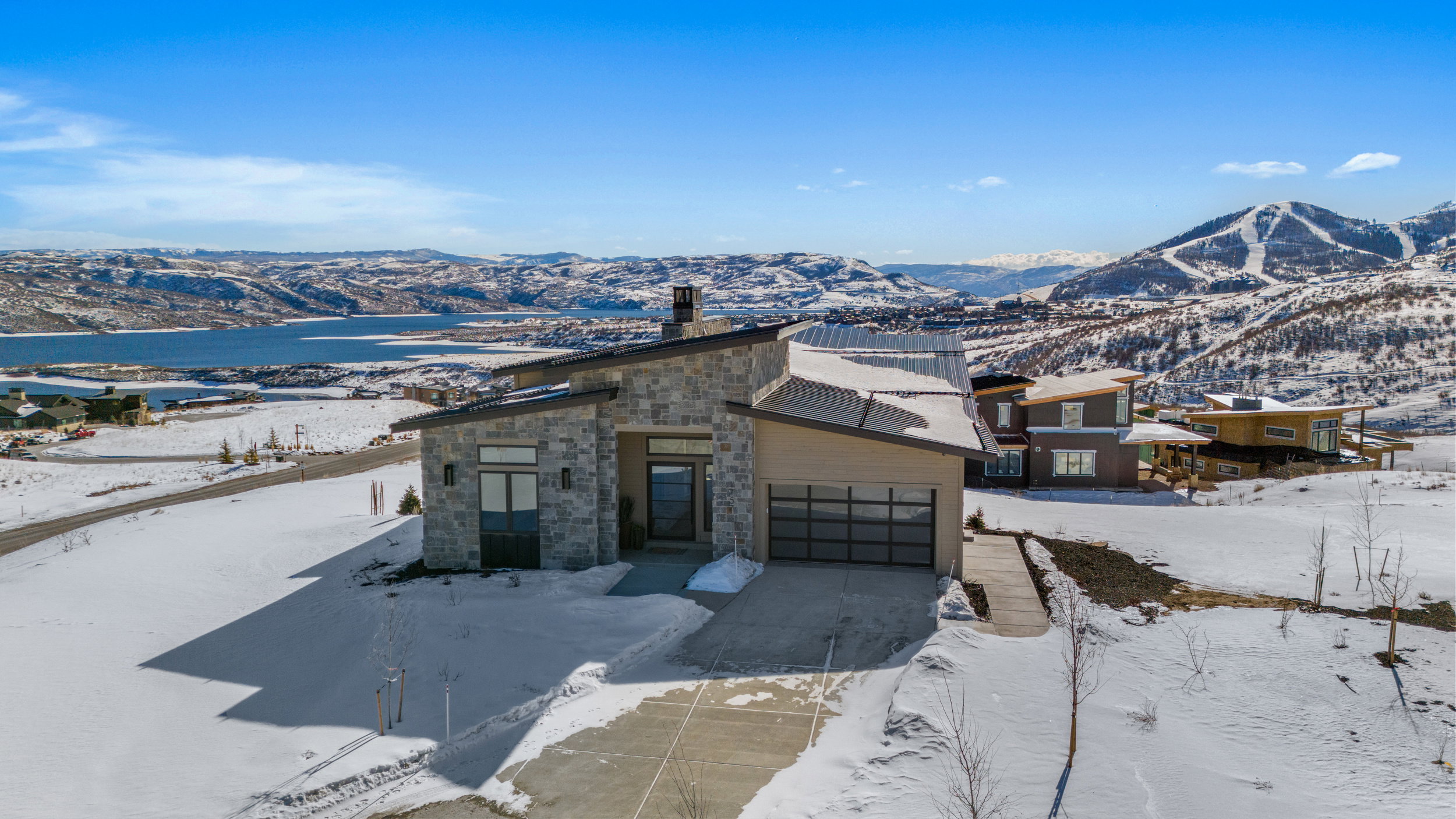 View of front facade featuring a mountain view, stone siding, a garage, a chimney, and driveway