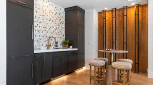 Indoor wet bar with light wood-type flooring, paneled built in refrigerator, light stone countertops, and recessed lighting