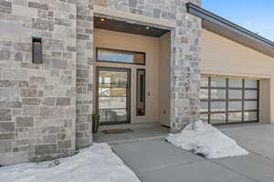 Property entrance with stone siding, a garage, and concrete driveway