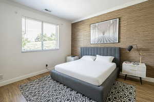 Bedroom with an accent wall, crown molding, wood finished floors, and wallpapered walls