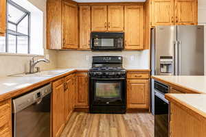 Kitchen featuring light countertops, black appliances, brown cabinetry, and light wood-style floors