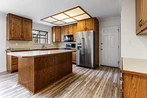 Kitchen featuring light countertops, brown cabinetry, ornamental molding, black appliances, and light wood-type flooring
