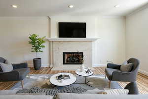 Living room with a high end fireplace, wood finished floors, ornamental molding, and recessed lighting