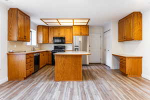 Kitchen featuring light countertops, brown cabinets, a center island, black appliances, and light wood-style flooring