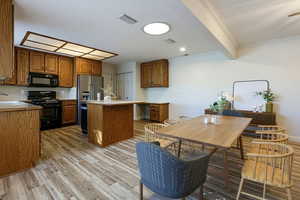 Kitchen with crown molding, brown cabinets, light countertops, black appliances, and a kitchen island