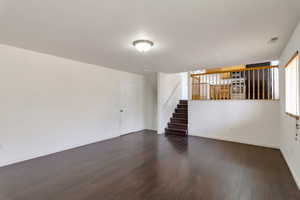 Unfurnished living room featuring dark wood-type flooring and stairs