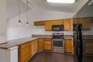 Kitchen featuring black appliances, decorative light fixtures, dark wood-type flooring, brown cabinetry, and lofted ceiling