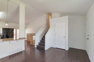 Unfurnished living room featuring dark wood-type flooring, stairs, and lofted ceiling