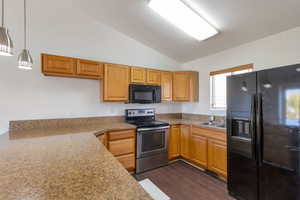 Kitchen featuring black appliances, vaulted ceiling, hanging light fixtures, dark wood-style floors, and light stone counters