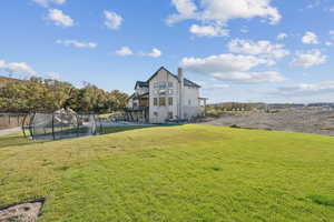 View of green lawn featuring a trampoline, a balcony, and stairway