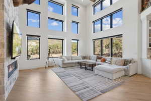 Living area featuring a stone fireplace, light wood-style flooring, and a high ceiling