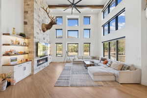 Living area featuring light wood finished floors, a large fireplace, beam ceiling, and ceiling fan