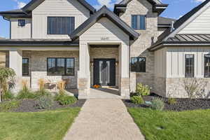 Doorway to property with board and batten siding, stone siding, a standing seam roof, a metal roof, and a porch