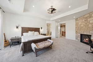 Bedroom featuring a raised ceiling, a fireplace, carpet flooring, recessed lighting, and a chandelier