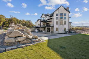 Rear view of house featuring stairway, board and batten siding, a balcony, a yard, and a patio