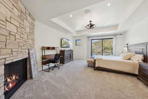 Bedroom featuring a tray ceiling, carpet floors, a stone fireplace, recessed lighting, and a desk