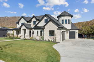 View of front of home featuring a front lawn, stone siding, board and batten siding, a standing seam roof, and concrete driveway