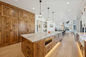 Kitchen featuring brown cabinets, hanging light fixtures, light stone counters, light wood-style floors, and recessed lighting