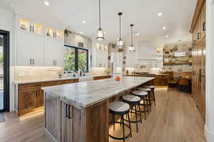 Kitchen featuring brown cabinetry, light wood-style flooring, light stone counters, a kitchen breakfast bar, and tasteful backsplash