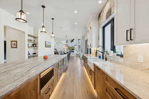 Kitchen with light stone countertops, hanging light fixtures, light wood finished floors, brown cabinetry, and open floor plan