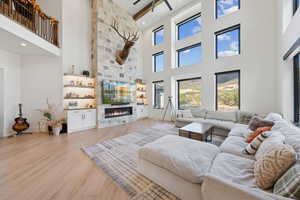 Living room with light wood-type flooring, a stone fireplace, a high ceiling, a ceiling fan, and recessed lighting