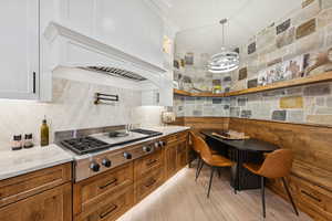 Kitchen featuring decorative light fixtures, stainless steel gas cooktop, light stone countertops, glass insert cabinets, and white cabinets