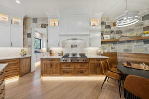 Kitchen featuring brown cabinetry, hanging light fixtures, light stone counters, and decorative backsplash