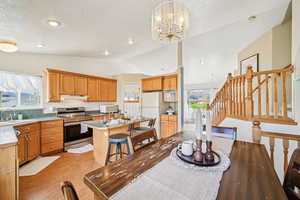 Dining room with light wood-style floors, stairway, a textured ceiling, lofted ceiling, and a chandelier