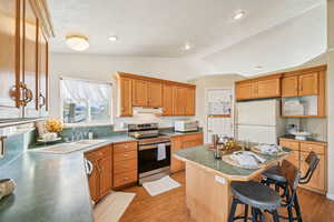 Kitchen featuring white appliances, a breakfast bar area, a kitchen island, light wood-type flooring, and a textured ceiling