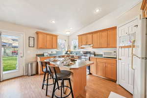 Kitchen with a breakfast bar area, white appliances, vaulted ceiling, light countertops, and light wood-style floors