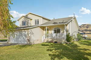 View of front of house with a porch, a front lawn, a shingled roof, and driveway with mountain and rural views.