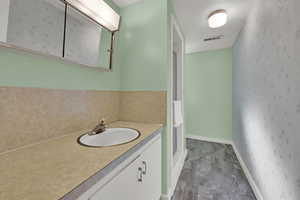 Full bath with wallpapered walls, a stall shower, and vanity