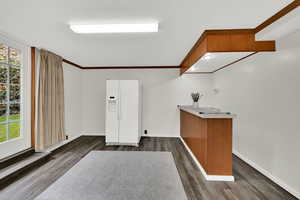 Bar area with crown molding, white refrigerator with ice dispenser, dark wood-style floors, brown cabinetry, and light countertops