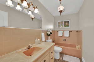Bathroom featuring a garden tub, vanity, tile walls, and a wainscoted wall