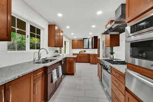 Kitchen featuring backsplash, a warming drawer, light stone countertops, appliances with stainless steel finishes, and brown cabinetry
