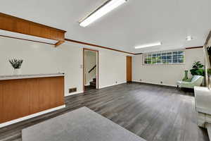 Basement with dark wood-type flooring, stairway, and ornamental molding