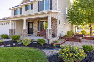 View of front of house featuring stone siding, a garden, a porch, and a garage