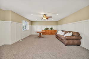 Living area featuring a decorative wall, wainscoting, recessed lighting, carpet, and ceiling fan
