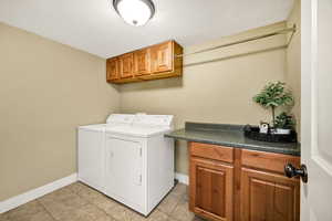 Washroom with cabinet space, light tile patterned floors, washer and clothes dryer, and a textured ceiling