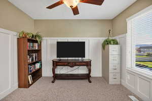 Sitting room with a decorative wall, wainscoting, light colored carpet, a ceiling fan, and plenty of natural light