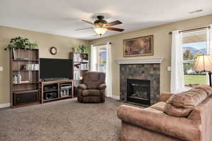Living area featuring carpet floors, a tiled fireplace, and ceiling fan