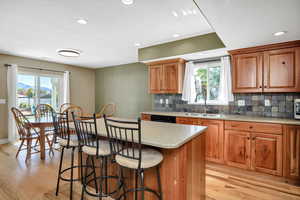 Kitchen with brown cabinetry, light wood-type flooring, backsplash, a kitchen breakfast bar, and recessed lighting