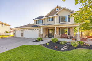 Craftsman house featuring covered porch, driveway, an attached garage, a front yard, and stone siding