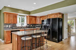 Kitchen with black appliances, brown cabinets, recessed lighting, a kitchen breakfast bar, and light wood finished floors
