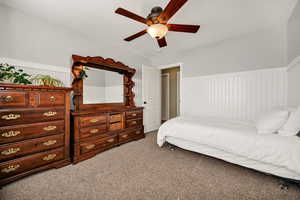 Bedroom with a wainscoted wall, light carpet, and ceiling fan