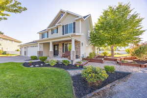 Craftsman-style home with covered porch, asphalt driveway, a front yard, a garden, and stone siding
