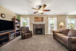 Carpeted living room with a tiled fireplace, healthy amount of natural light, and ceiling fan