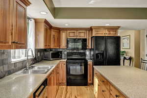 Kitchen with black appliances, light wood finished floors, backsplash, brown cabinetry, and recessed lighting