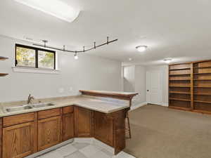 Bar with brown cabinetry, a textured ceiling, open shelves, and light colored carpet