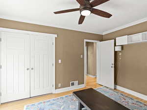 Bedroom with a closet, crown molding, wood floors, and a ceiling fan